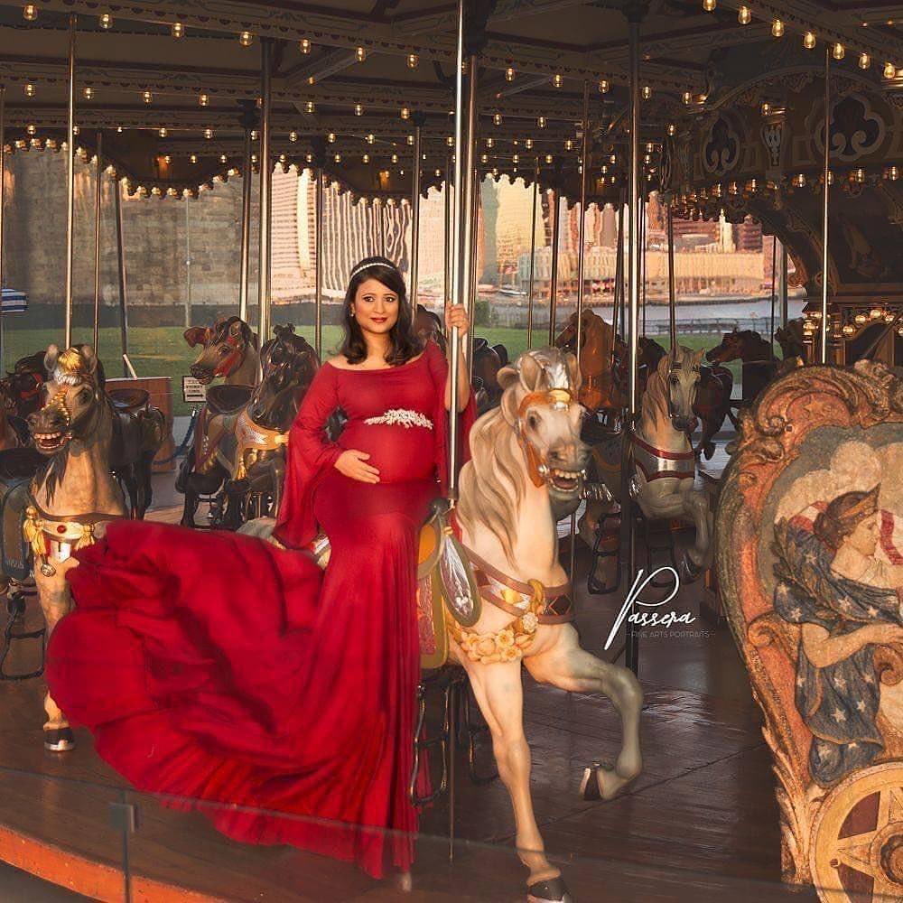 Pregnant woman in long red dress on a carousel horse