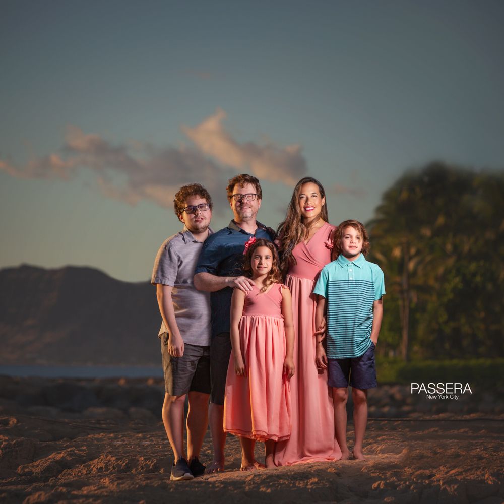 A mom, dad, and 2 sons and a daughter standing on  the beach with a dark backdrop