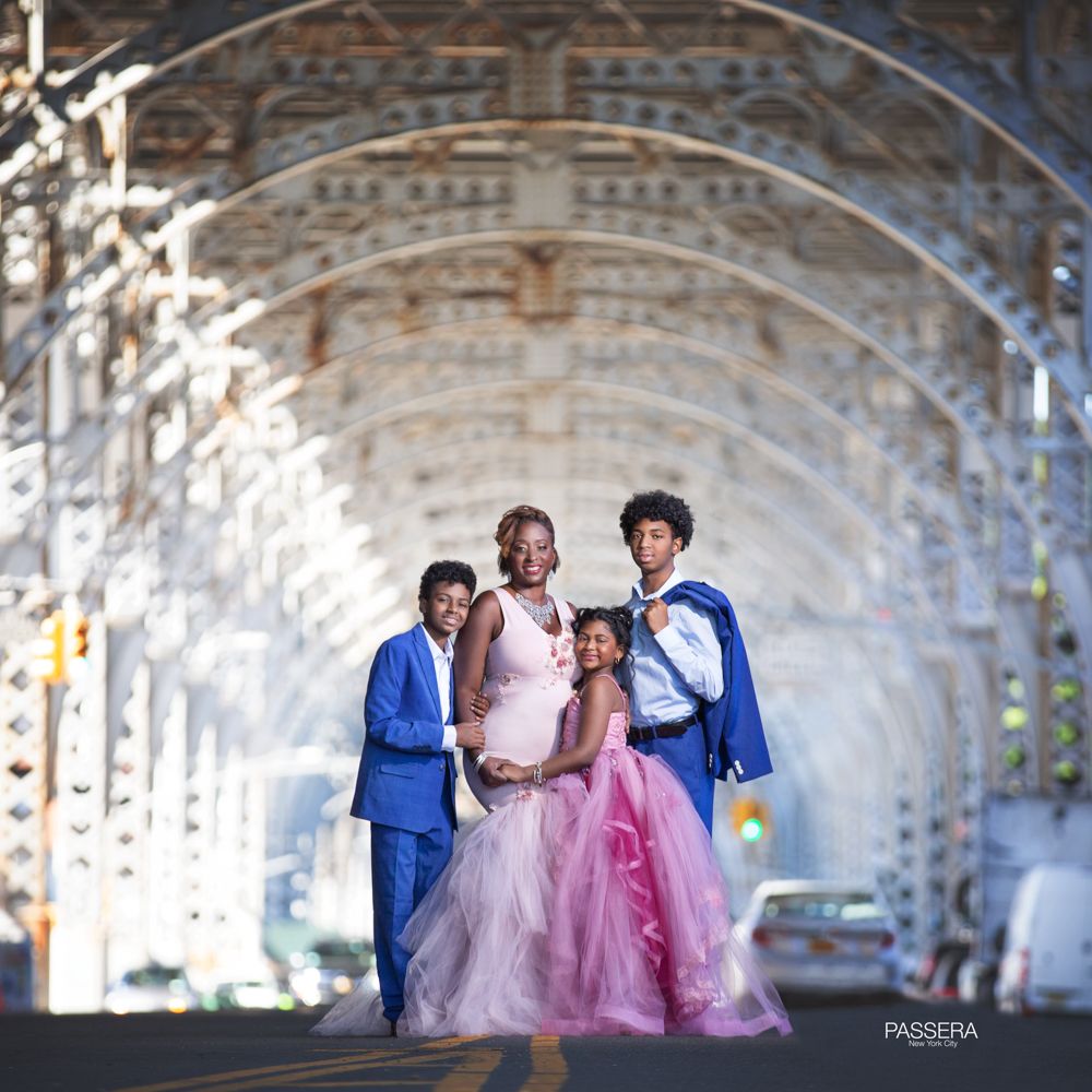 African American mom with 3 children - 2 boys and a girl standing in a tunnel like object. They are all dress in formal wear. The 2 boys are dressed in blue, while the mom and daughter are dressed in pink.