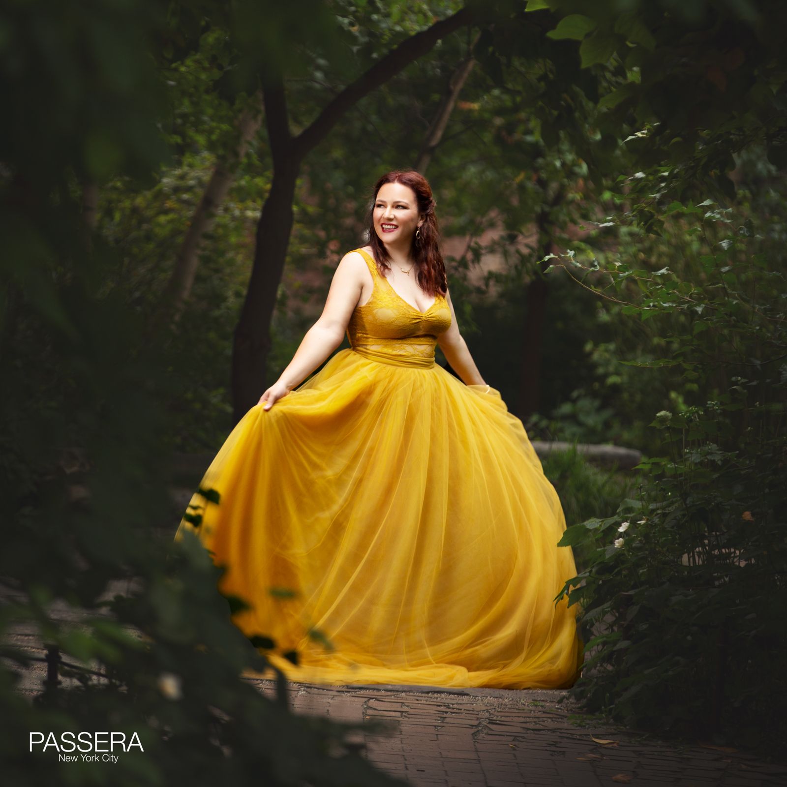 white skinned woman with dark brunette hair pinned up-- in a forest background - standing up with her hands to the side holding her beautiful yellow ball gown dress.